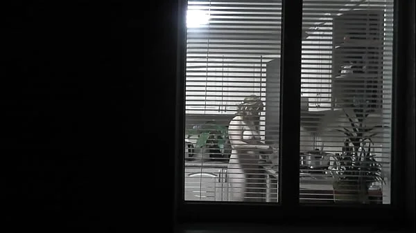 Peeping. Voyeur. Neighbor pervert voyeur in evening on street looks out window as naked sexy neighbor in kitchen prepares dinner for her husband. Naked in public. Naked at home. Family.  Outdoor